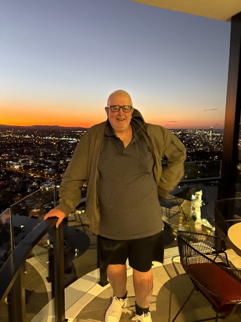 A man standing on a high-rise balcony at sunset with the city skyline behind him